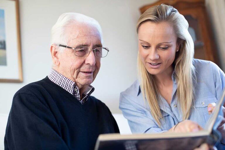 Grandfather Looking At Photo Album With Adult Granddaughter