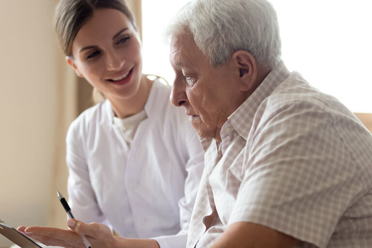 Older man patient and young nurse talking indoors