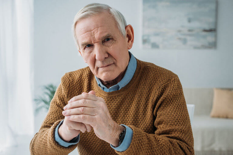 Senior thoughtful man sitting by the desk in light