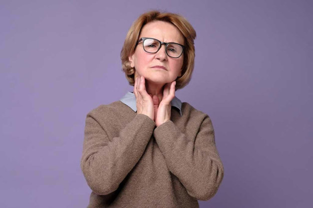 Senior woman in glasses touching painful neck, sore throat for flu, cold and infection Senior woman in glasses touching painful neck, sore throat for flu, cold and infection