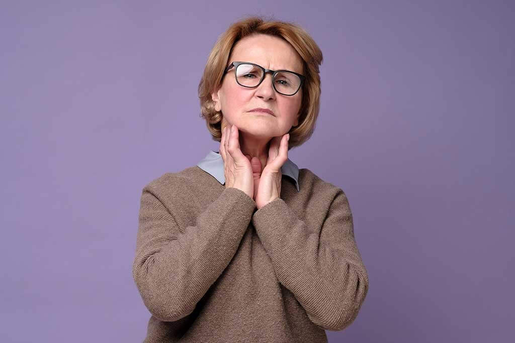 Senior woman in glasses touching painful neck, sore throat for flu, cold and infection Senior woman in glasses touching painful neck, sore throat for flu, cold and infection