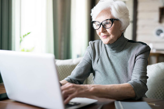 White haired senior woman wearing eyeglasses sitting at cafe and using her laptop White haired senior woman wearing eyeglasses sitting at cafe and using her laptop