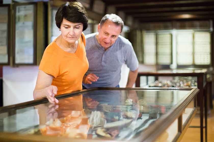 cheerful senior couple examining objects applied art in museum
