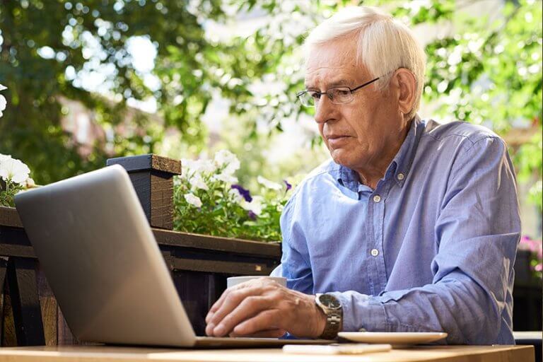 Portrait of senior man working with laptop in outdoor cafe lounge