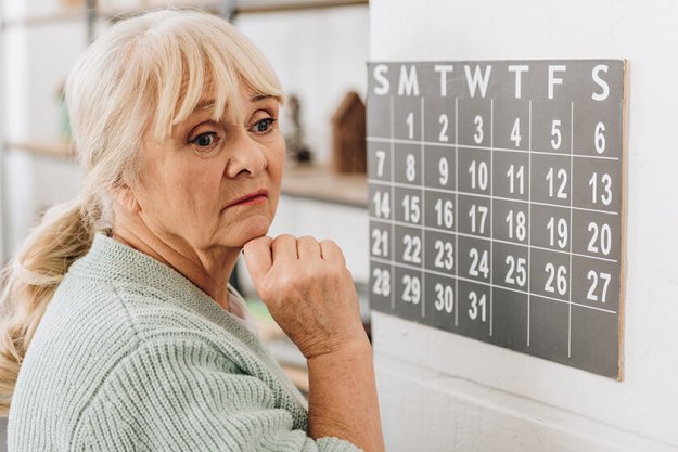 upset senior woman touching wall calendar and remembering dates