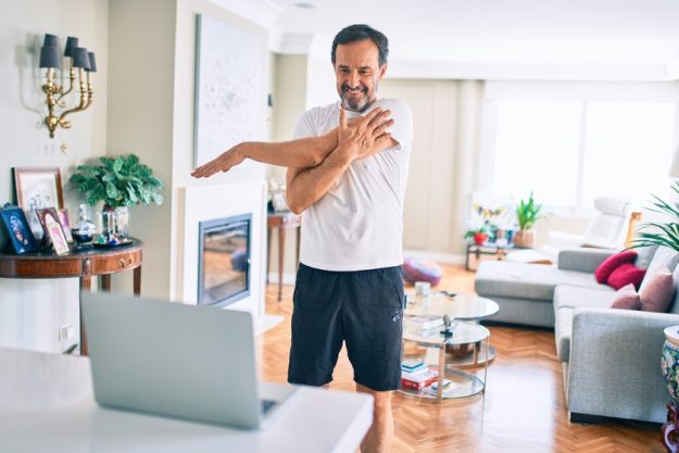Middle age man with beard training and stretching doing exercise at home looking at sport video on computer