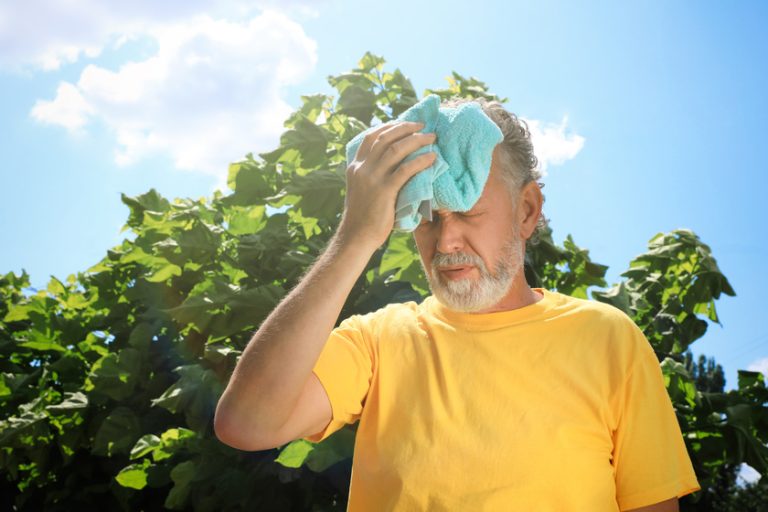 Senior man with towel suffering from heat stroke outdoors, space