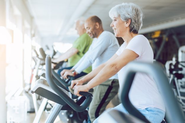 Fit seniors on stationary fitness bikes in the gym Fit seniors on stationary fitness bikes in the gym