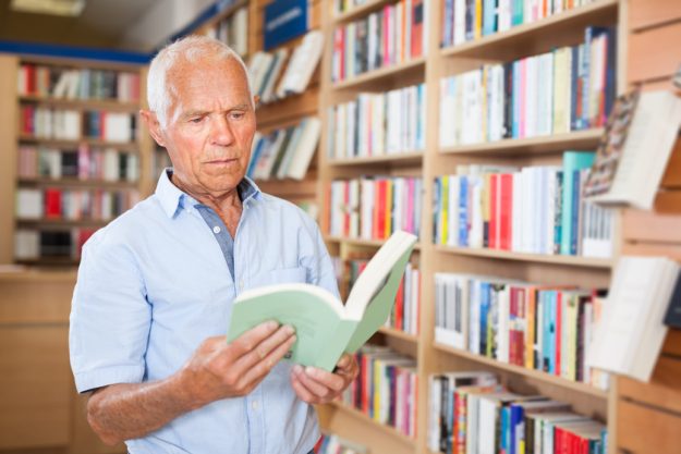 Intelligent older male browsing inside of books while visiting l