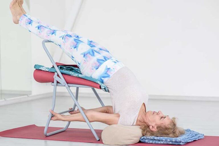 Senior woman doing yoga with chair at studio. Stretching exercises