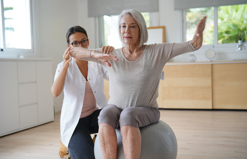 Senior woman exercising with her physiotherapist and swiss ball