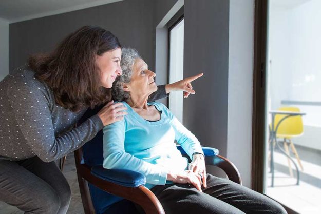 Adult daughter showing to senior mother scene out of window