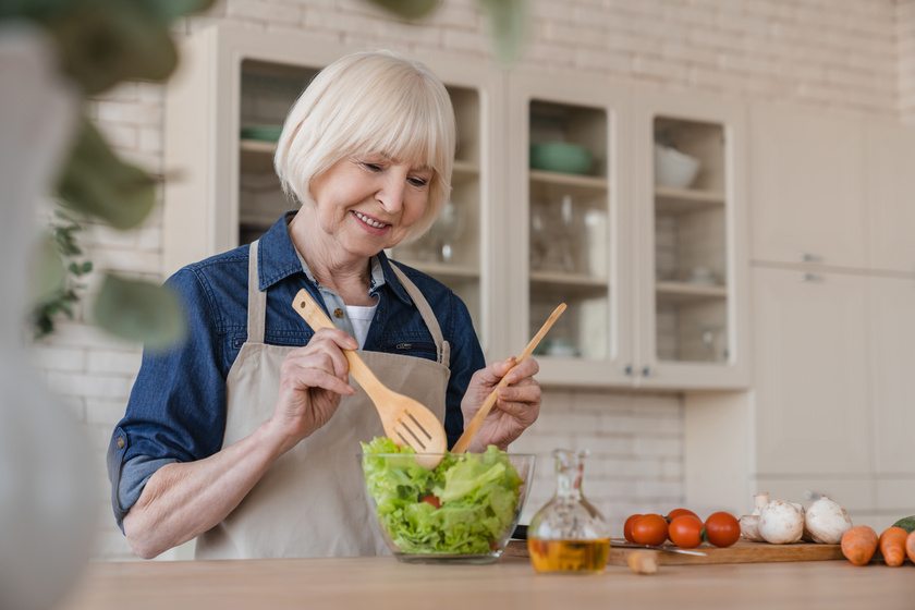 Old aged elderly senior caucasian woman grandmother mixing ingredients in vegetable salad, cooking healthy food at home, preparing meal at home. Dieting and active seniors concept