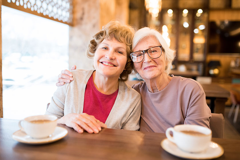 Cheerful positive attractive senior lady friends sitting at table with cups