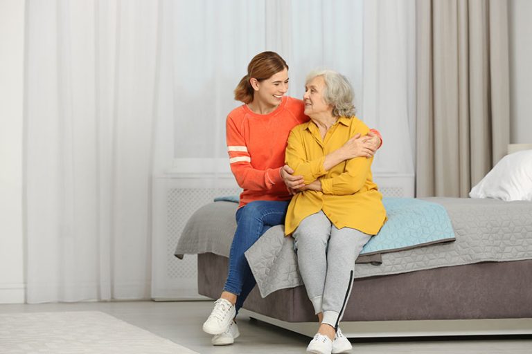Elderly woman with female caregiver in bedroom. Space for text