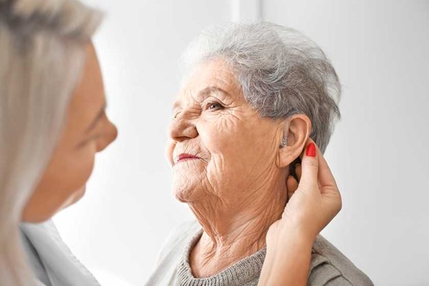 Otolaryngologist putting hearing aid in senior woman's ear
