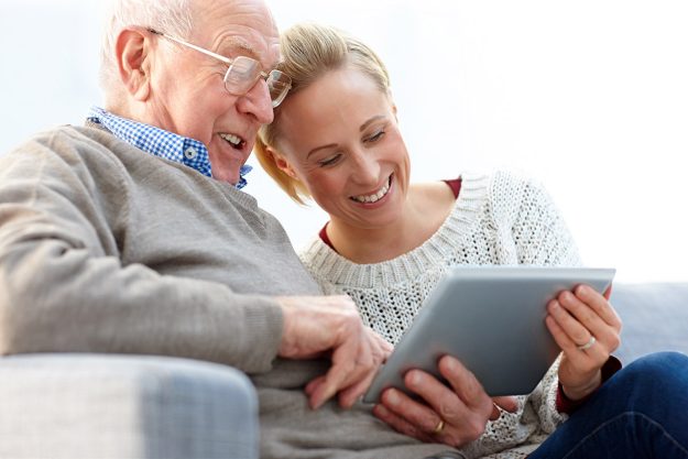 Happy father and daughter sitting on sofa using digital tablet – Indoors What Are The Main Responsibilities Of A Caregiver In A Metairie, LA Assisted Living Home?
