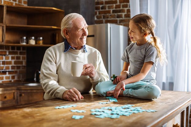 Joyful aged man assembling jigsaw puzzles with his granddaughter Joyful aged man assembling jigsaw puzzles with his granddaughter