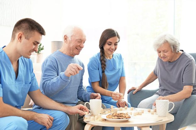 Senior people playing bingo with their caregivers indoors