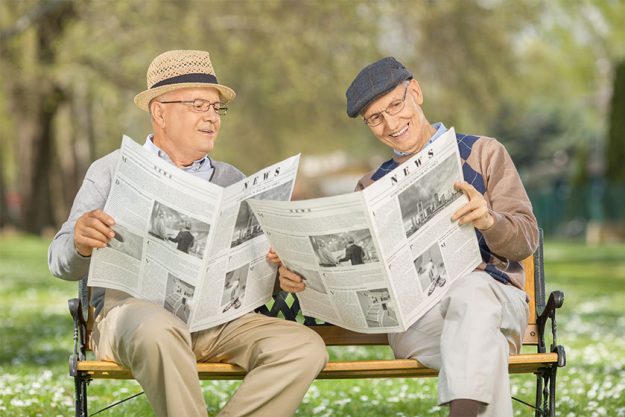 Seniors reading newspaper in a park Seniors reading newspaper in a park