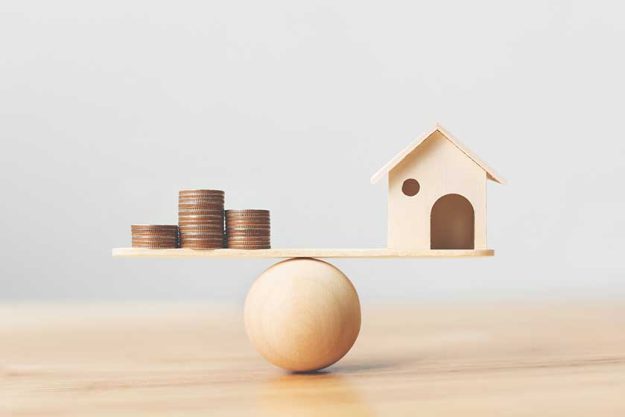 Wooden home and money coins stack on wood scale Wooden home and money coins stack on wood scale