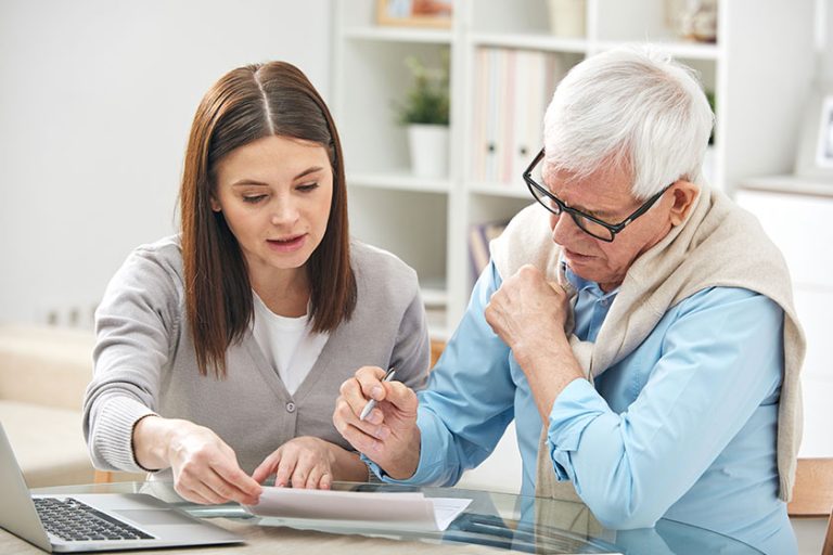 Young female explaining her senior father how to fill in paper