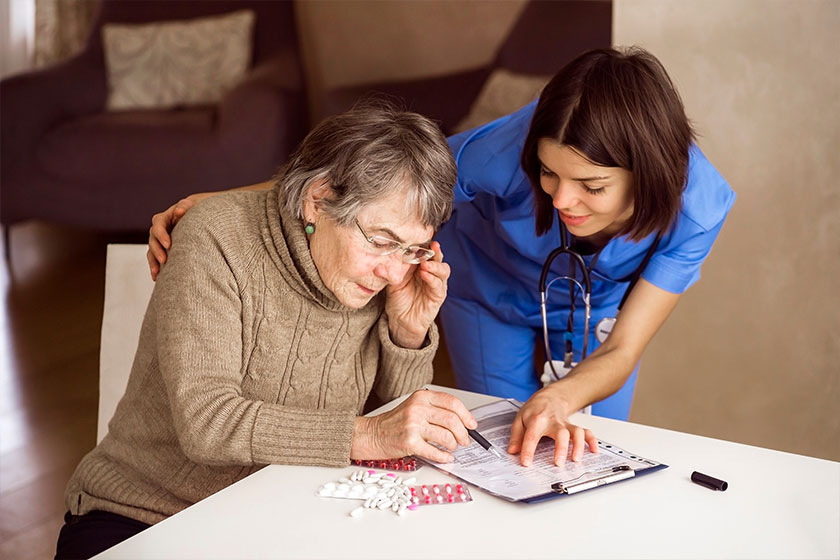 An elderly gray-haired woman with glasses reads a health insurance contract and signs it