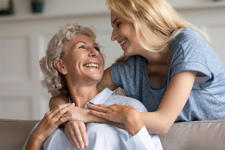 Elderly mom sit on sofa while adult grown up daughter hugs her from behind