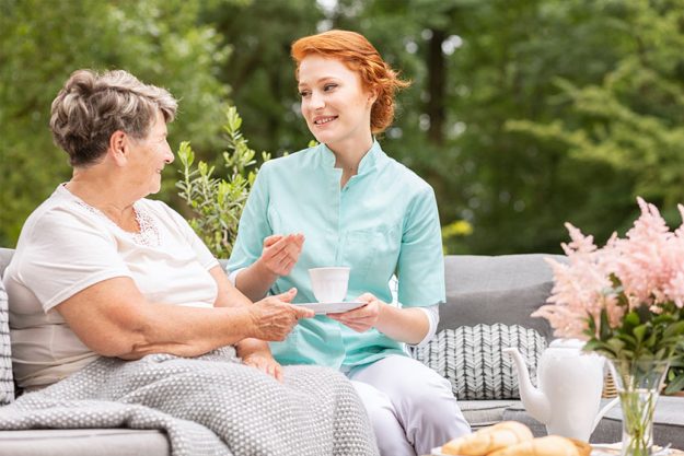 Friendly caregiver with tea talking with senior woman in the garden