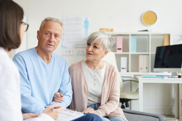 Portrait of modern senior couple listening to female doctor while visiting clinic