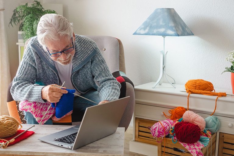 Smiling senior man enjoying knitting at home