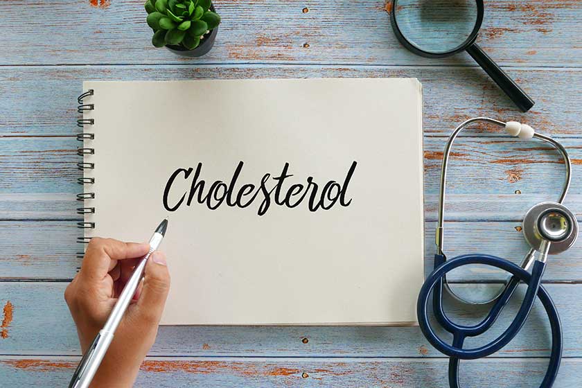 Top view of stethoscope,magnifying glass,plant and hand holding pen writing Cholesterol on notebook Top view of stethoscope,magnifying glass,plant and hand holding pen writing Cholesterol on notebook