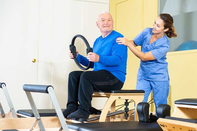 Young female doctor of rehabilitation center helping elderly man