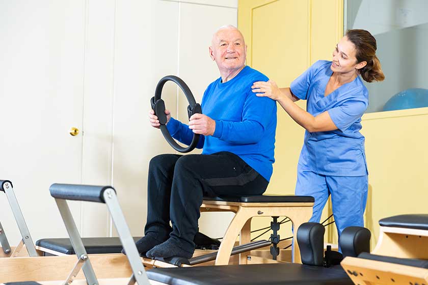 Young female doctor of rehabilitation center helping elderly man