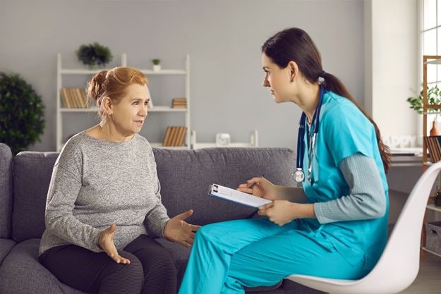 Young general practitioner with clipboard listening to senior female patient during home visit Young general practitioner with clipboard listening to senior female patient during home visit