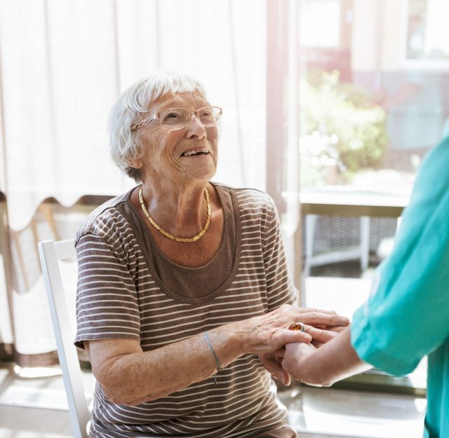 Smiling senior woman holding hands of healthcare worker at nursing home