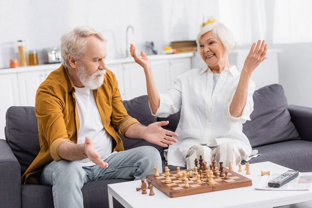 Senior Man Pointing Hands Chess Boars Smiling Wife Couch