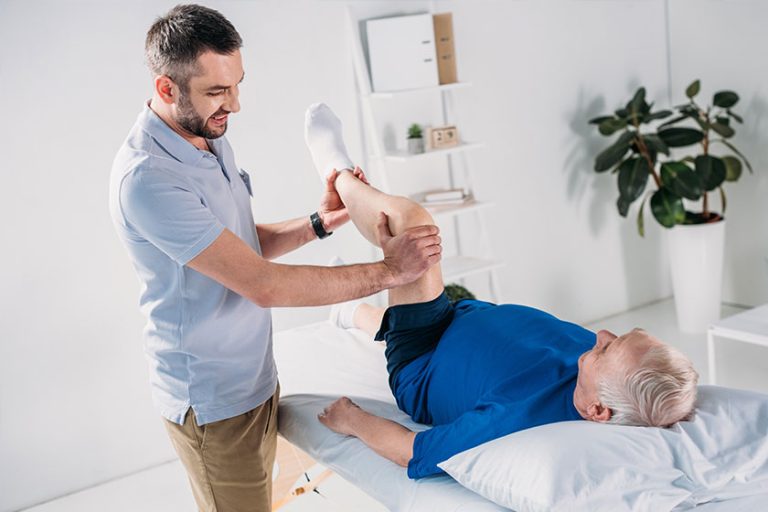 Smiling Physiotherapist Massaging Senior Mans Leg Massage Table
