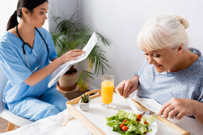 Senior Woman Having Breakfast Young Asian Nurse Reading Newspaper