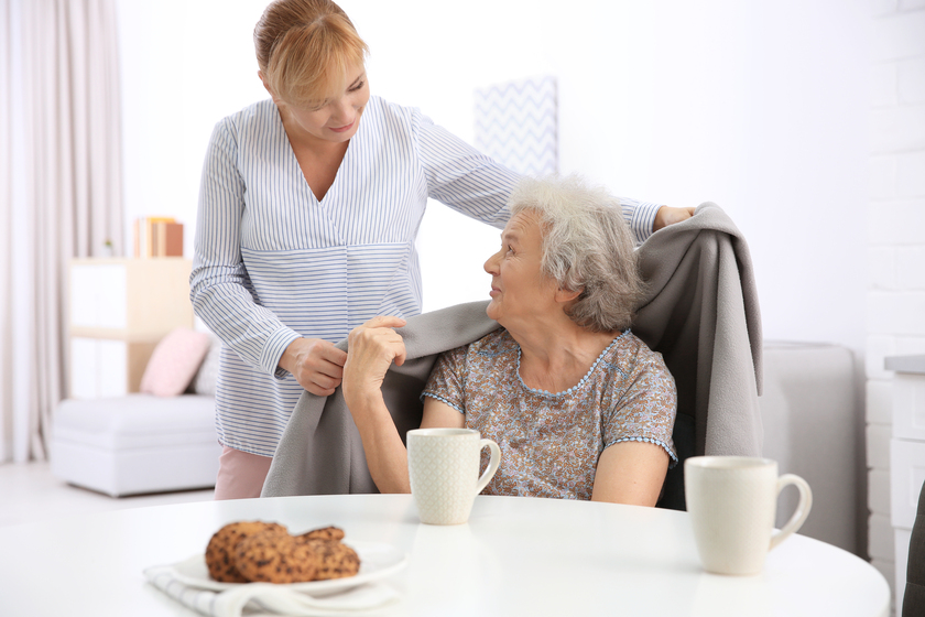 Caregiver covering senior woman with plaid at home