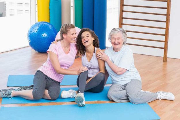 Playful friends sitting on exercise mat in gym Playful friends sitting on exercise mat in gym
