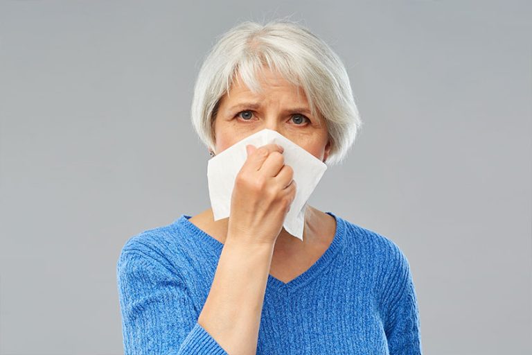 Sick senior woman blowing nose to paper napkin