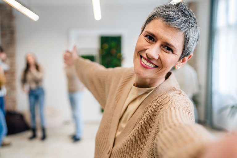 Portrait of senior woman in front of group of people men and women colleagues portrait of caucasian female stand at work happy smile confident with short gray hair copy space bright filter