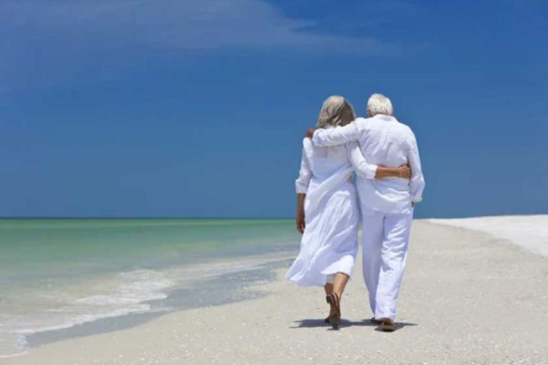 Rear View of Senior Couple Walking Alone on A Tropical Beach