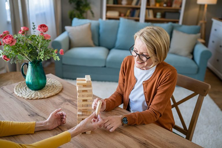 Two senior women female woman friends or family sisters play leisure board game at home have fun pensioner grandmother spend time together with their mature daughter