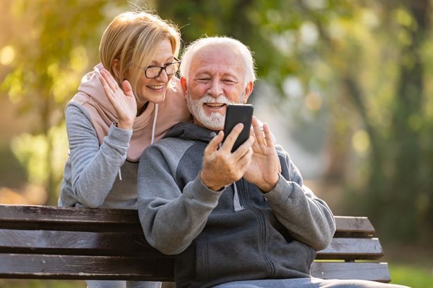 Elderly couple using mobile phone sitting on the bench