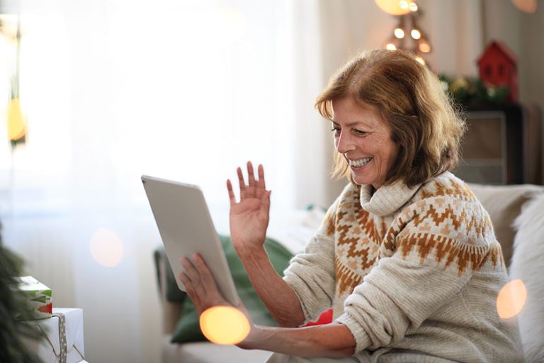 side view of senior woman indoors at home at christmas having video call with family