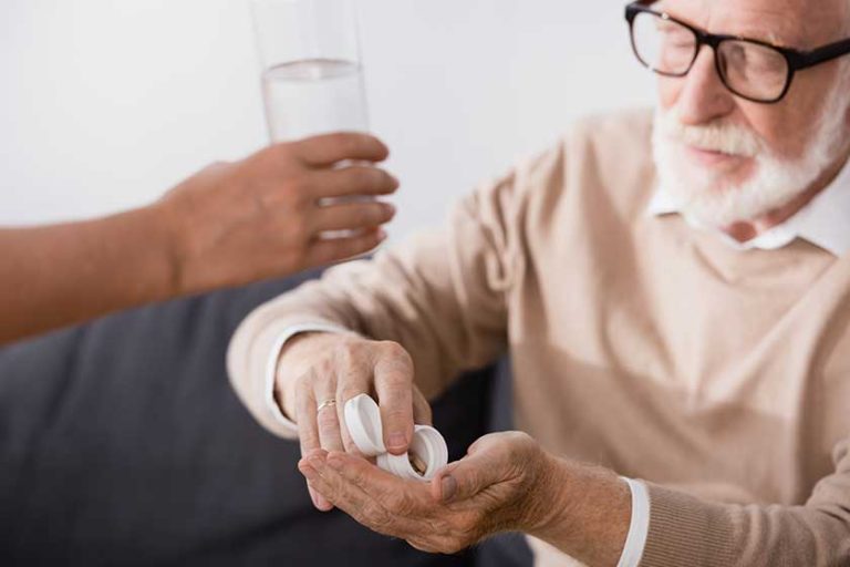 elderly man eyeglasses taking pills nurse giving glass water blurred