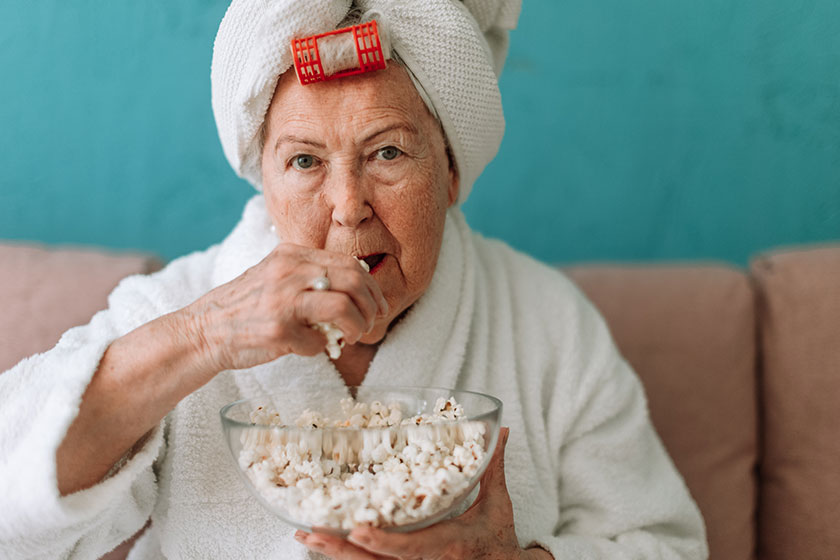 happy senior couple sitting sofa bathrobes watching popcorn