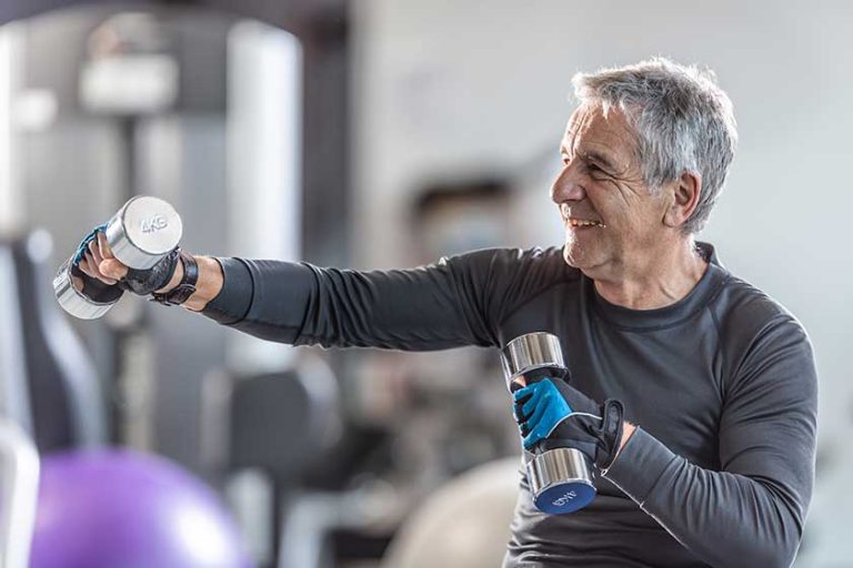 older man working out dumbbells gym smiling